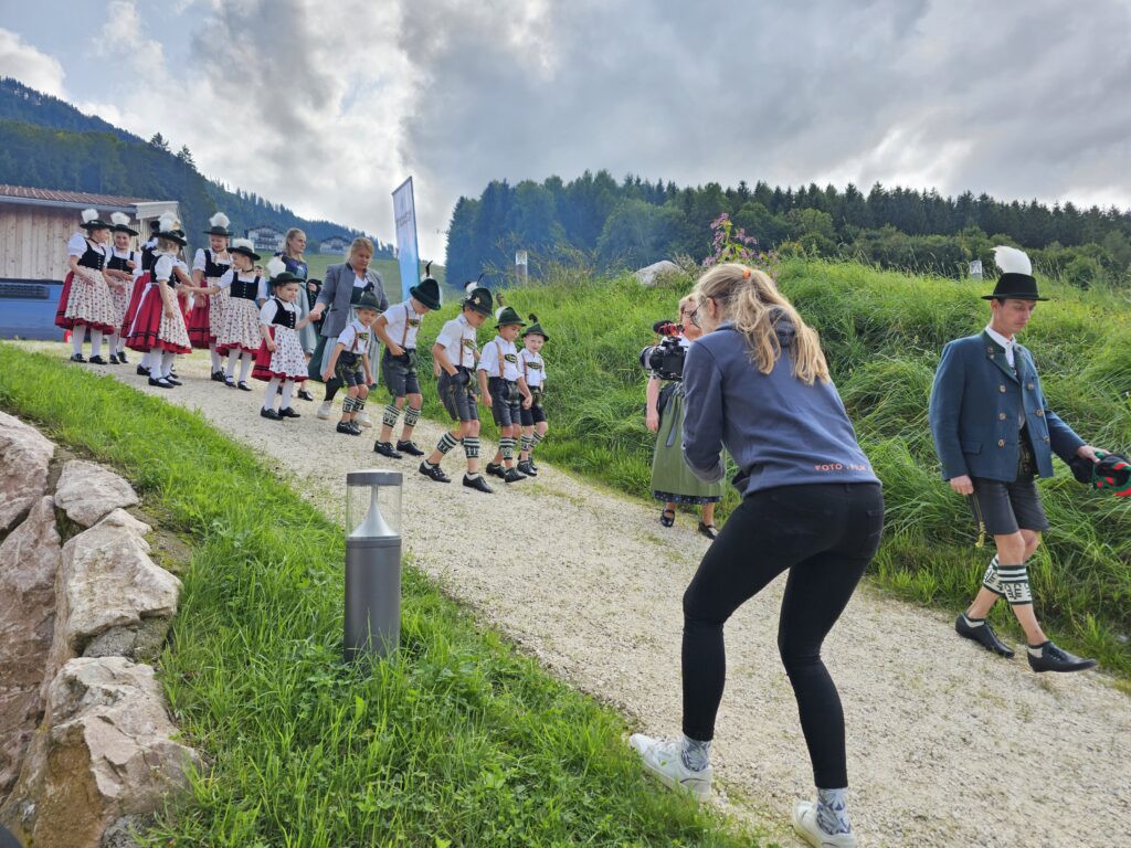 A photographer crouches to take pics of a troupe of tiny Bavarian-dressed children