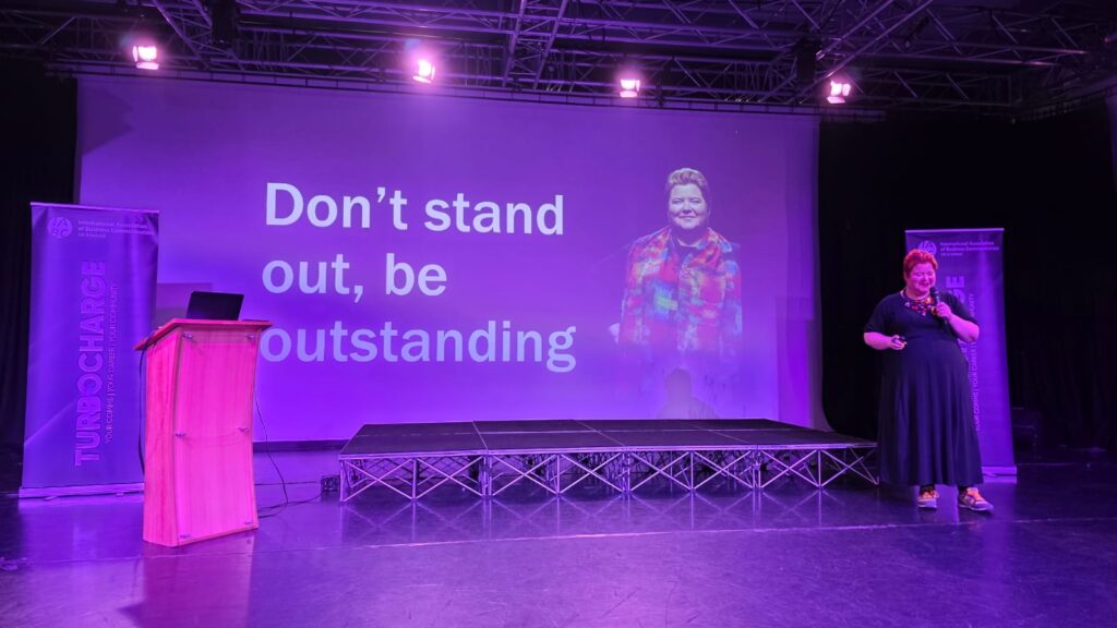 Woman standing in front of a slide that says don't stand out, be outstanding