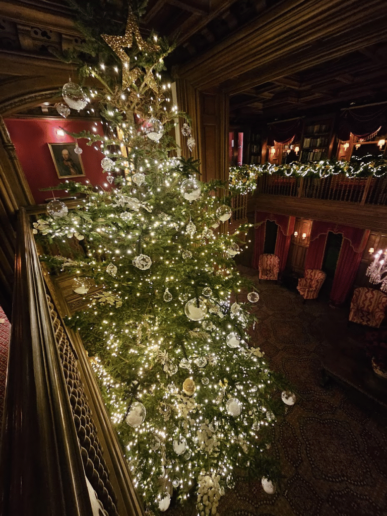Beautiful enormous Christmas tree bedecked with white lights and tasteful decorations. It's in a big room in an old castle and it is as high as the first floor / gallery view