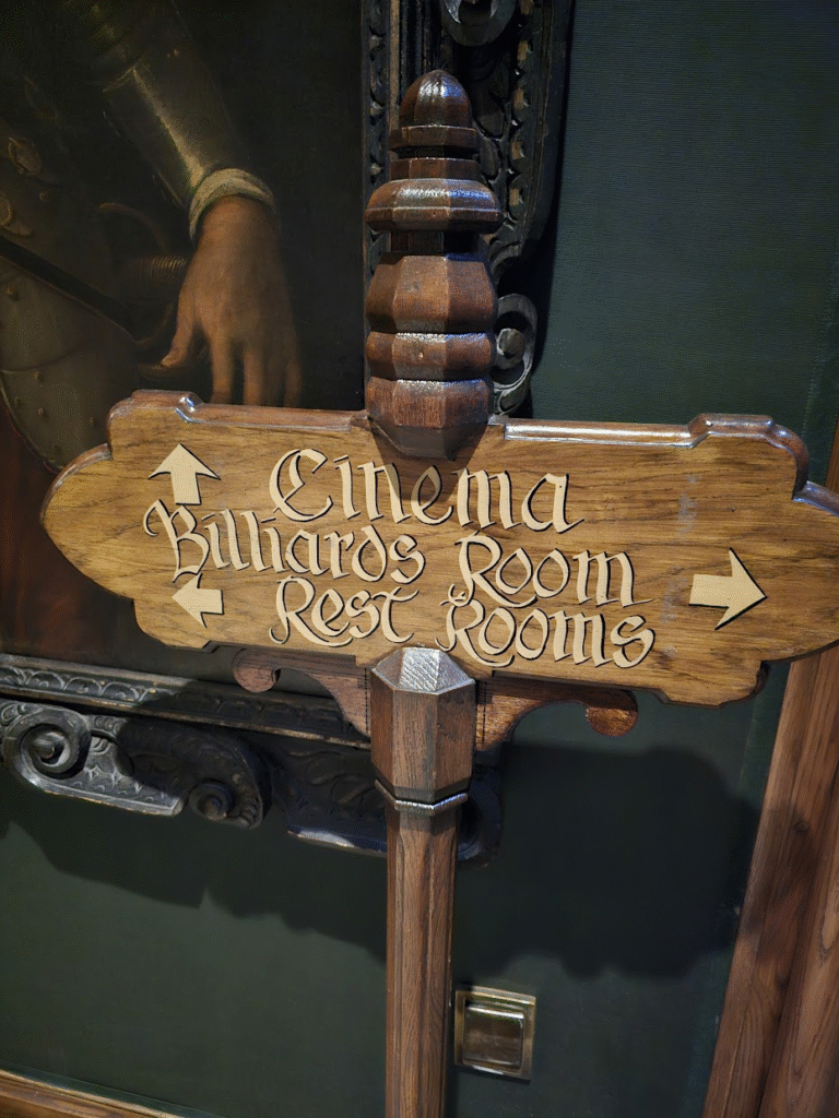Hand lettered wooden old-timey looking sign with cinema, billiards and rest rooms